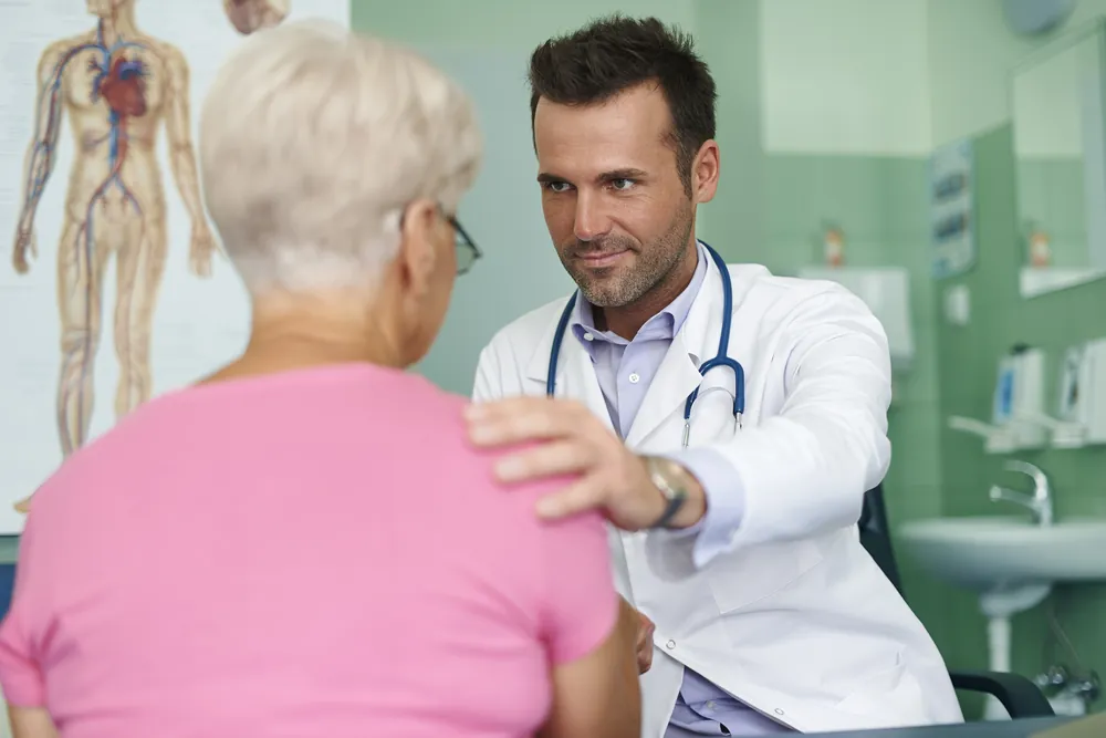 Capsulite rétractile : un médecin en blouse pose la main sur l’épaule d’une patiente âgée pendant la consultation.