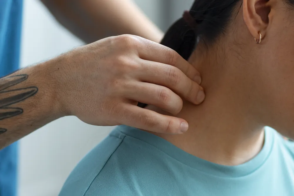Cervicalgie : un soignant palpe la nuque d’une patiente pour localiser la douleur cervicale.