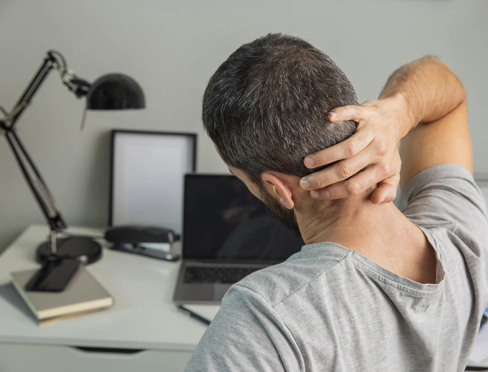 Homme vu de dos à son bureau, la main posée sur la nuque, étirant les muscles du cou et du haut du dos.