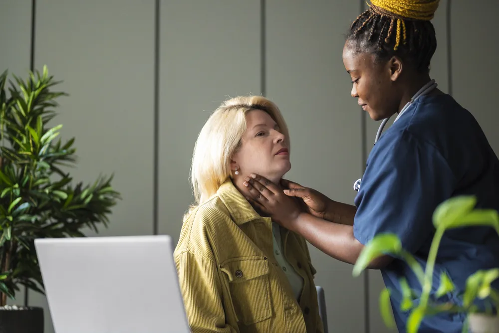 Cytoponction thyroïdienne : une soignante palpe le cou d’une patiente assise pour repérer la thyroïde avant l’examen.