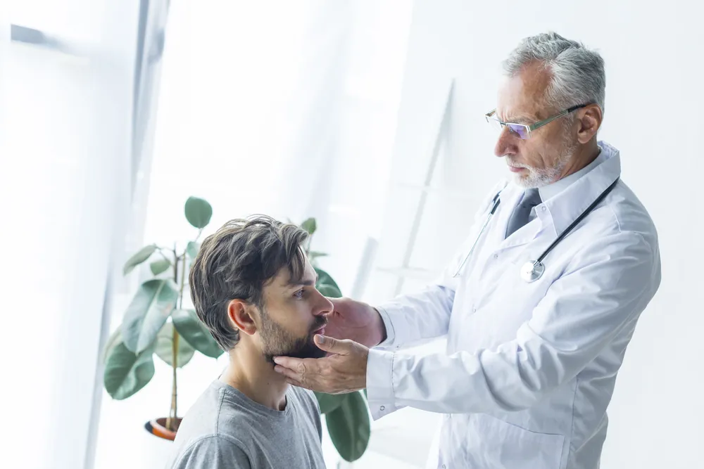 Échographie thyroïdienne : un médecin palpe le cou d’un patient assis avant l’examen.