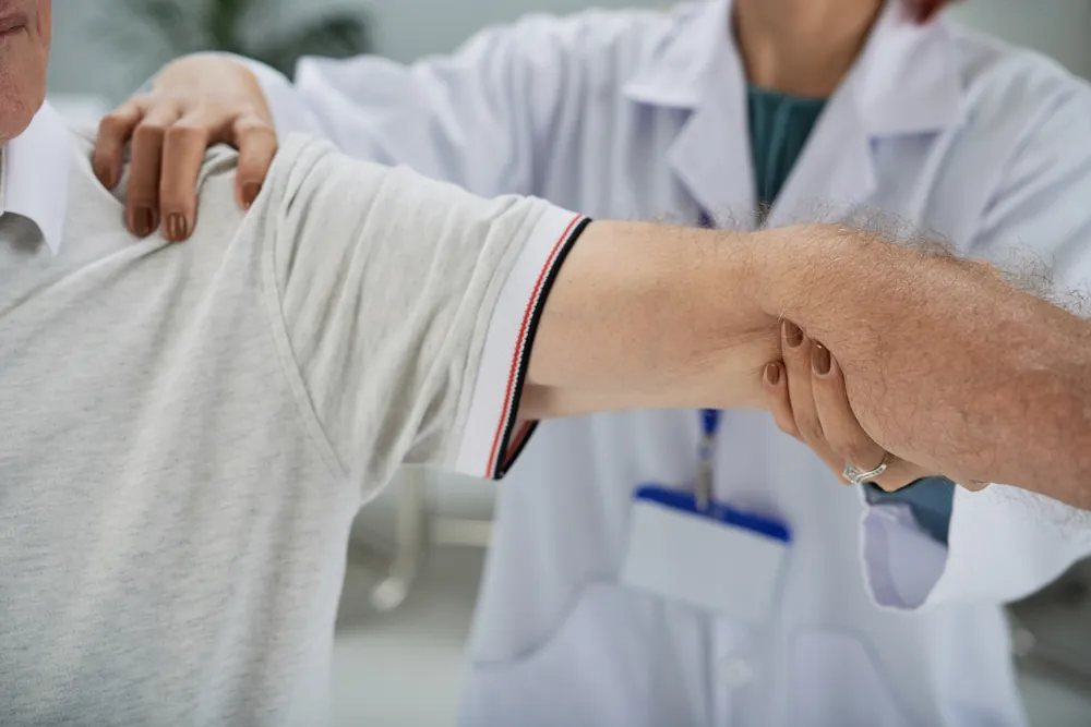 Épicondylite : une médecin en blouse examine le bras tendu d’un patient, une main sur son épaule, l’autre sur son avant-bras.