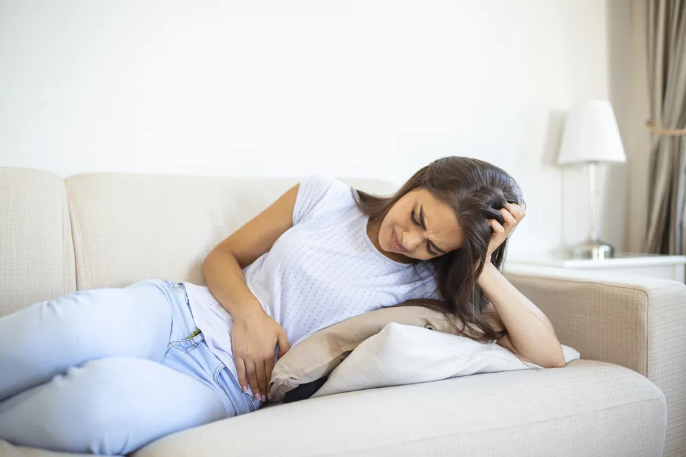 Fibrome utérin : une femme allongée sur un canapé se tient le bas-ventre, le visage crispé par la douleur.