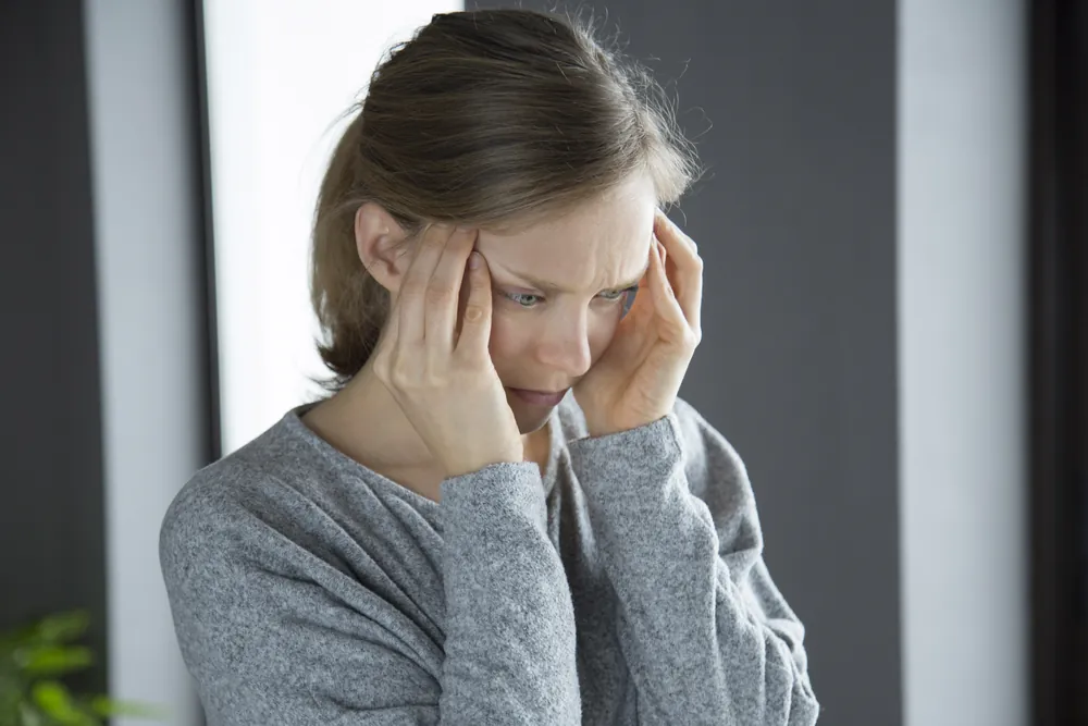 Névralgie d’Arnold : une femme se masse les tempes, le visage crispé par la douleur.