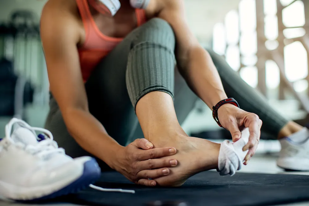 Névrome de Morton : une femme assise au sol en tenue de sport, chaussure retirée, se tient le pied douloureux.