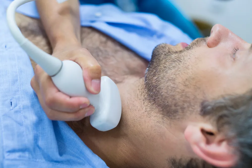 Échographie de la thyroïde : la sonde est posée sur le cou d’un patient allongé, la tête basculée en arrière.