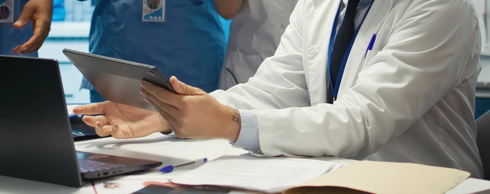 Équipe médicale de nos centres réunie autour d’un bureau : un médecin en blouse consulte une tablette, entouré de soignants en tenue.