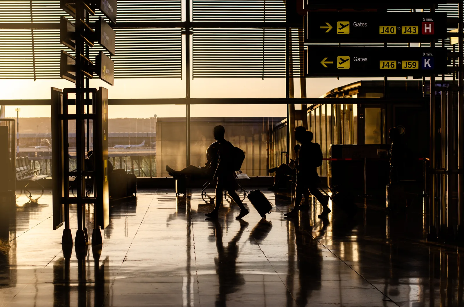 Voyageurs traversant un terminal d’aéroport avec leurs valises, en contre-jour.