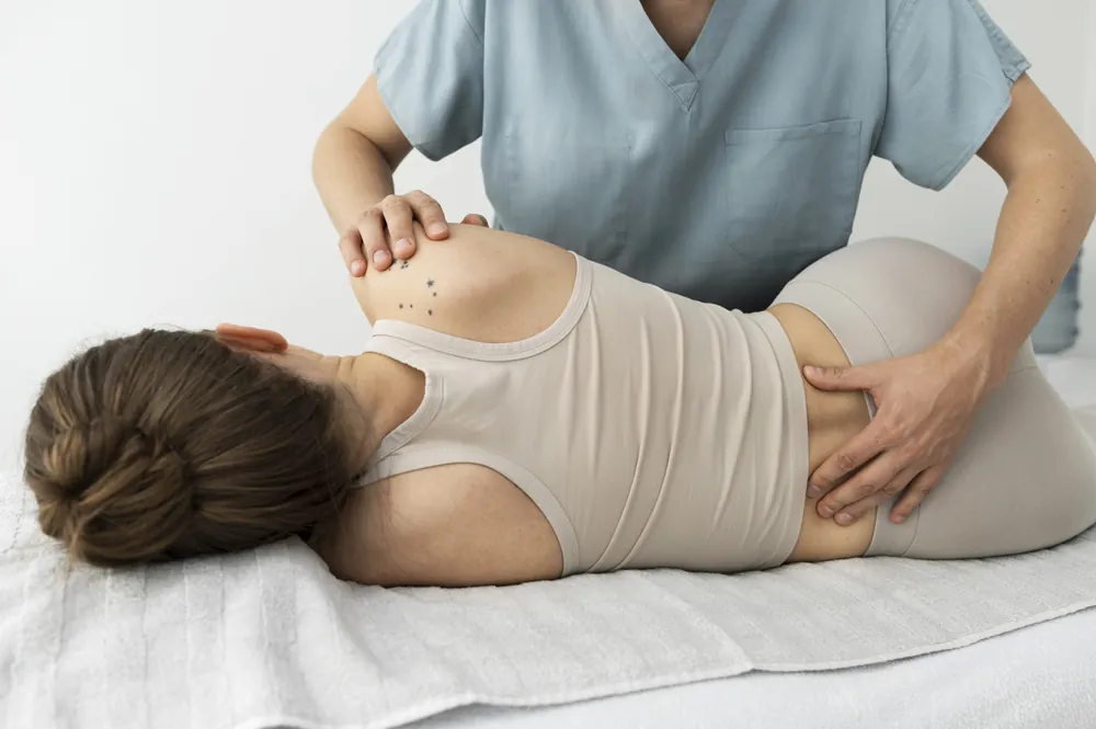 Syndrome du piriforme : une soignante examine la hanche et le bas du dos d’une patiente allongée sur le côté.
